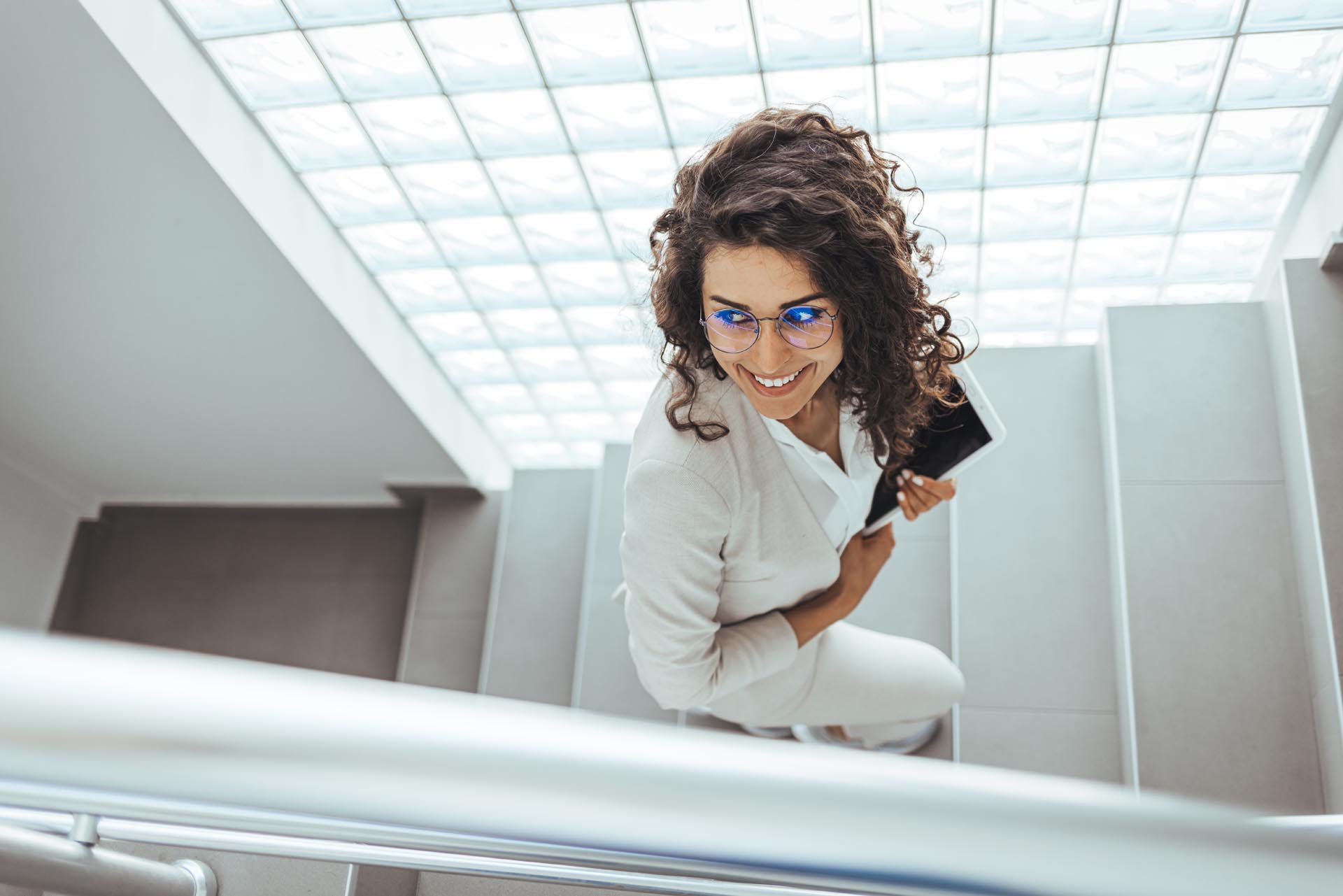 Portrait of young Caucasian businesswoman wearing high-heeled shoes walking upstairs and using digital tablet. Business concept. Cute young businesswoman walking up stairs